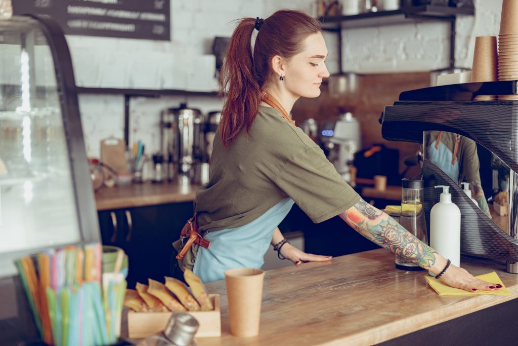 Young woman barista cleaning counter in cafe